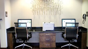 A dual-monitor workstation with two office chairs, a printer, and a decorative wall piece. - Hampton Inn Tampa/Rocky Point-Airport (Tampa)