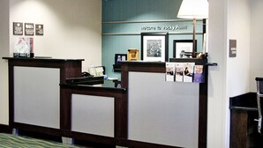 A reception desk with a blue wall and a welcome sign, a lamp, and a trash can. - Hampton Inn Tampa/Rocky Point-Airport (Tampa)