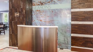 A reception desk with a modern design, a glass wall with a 'SEASONS' sign, and a brick-patterned wall. - DoubleTree by Hilton Atlanta Airport (Atlanta)