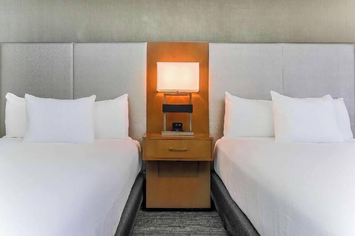 A hotel room with two beds, a nightstand with a lamp, and a headboard.
