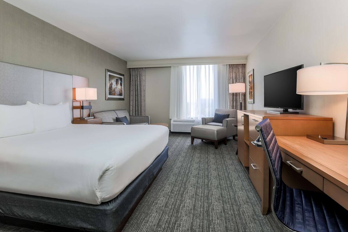 A hotel room with a large bed, a desk with a computer, a TV, and a chair.