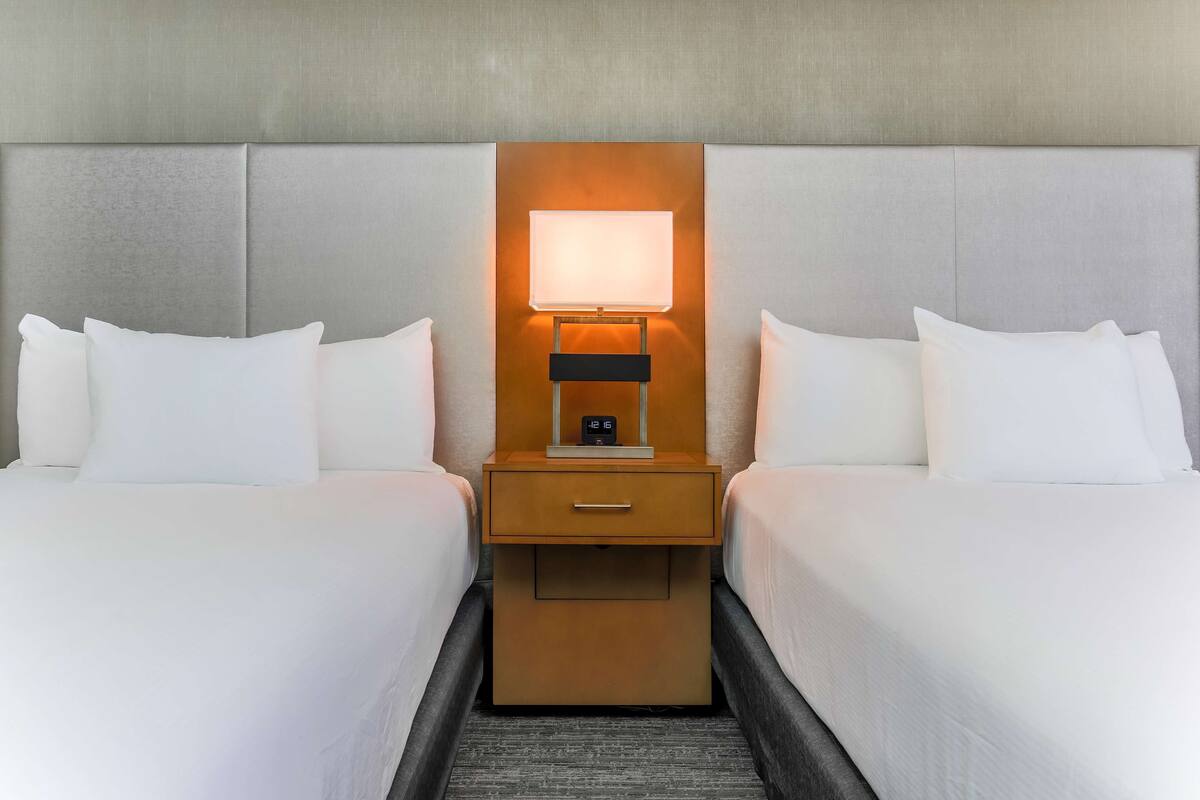 A hotel room with two beds, a nightstand with a lamp, and a clock.