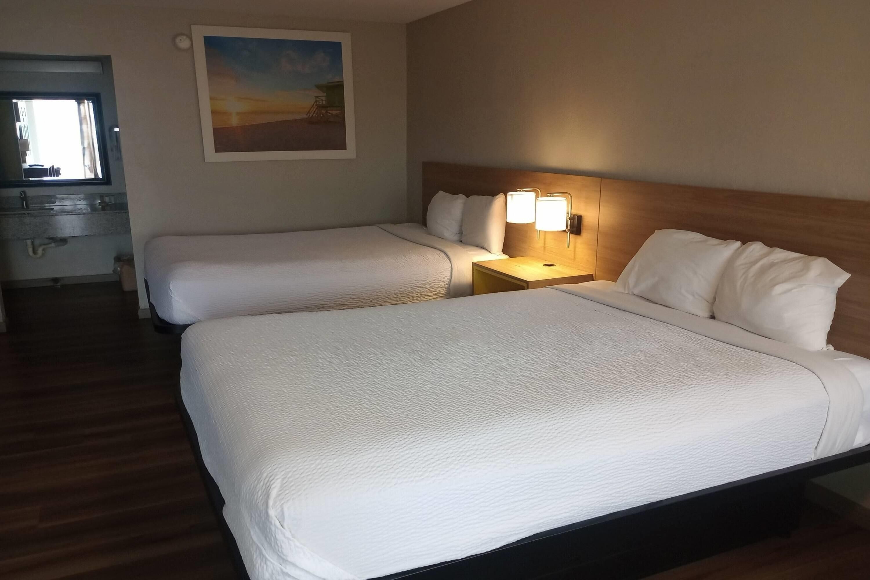 Et hotelværelse med to senge, et natbord med lampe, et billede på væggen og et vindue.