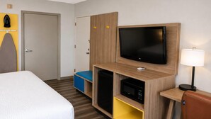 Ett hotellrum med en säng, en TV, en mikrovågsugn, ett litet kylskåp, ett skrivbord och en stol.