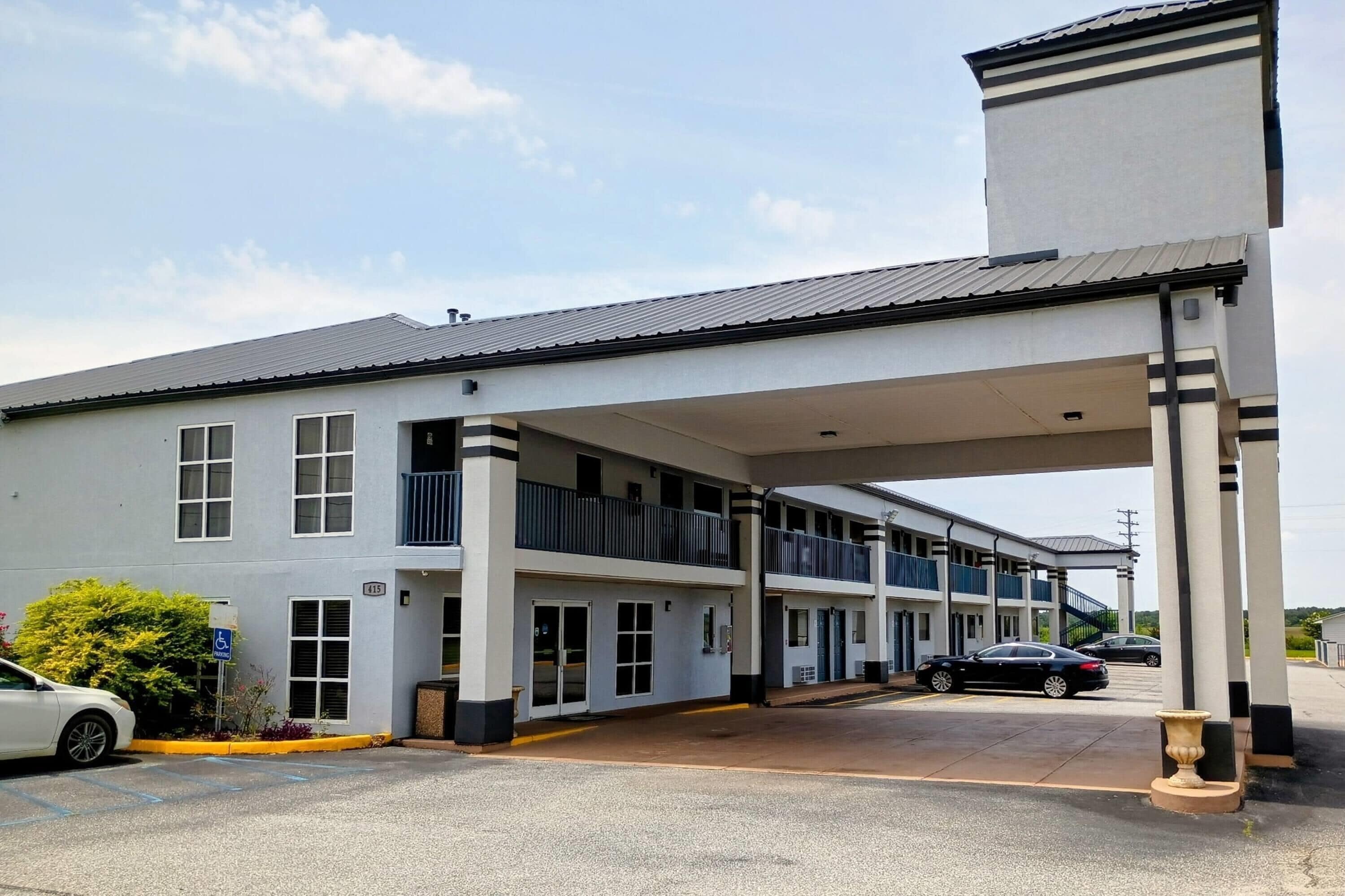 A multi-story motel with a covered parking area, a handicap-accessible entrance, and a visible car in the lot.