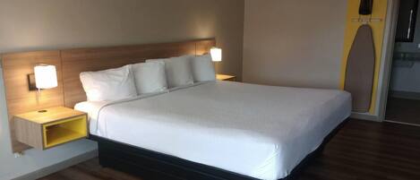 Una habitación de hotel moderna con una cama grande, mesitas de noche con lámparas, un cabecero de madera y una plancha integrada.