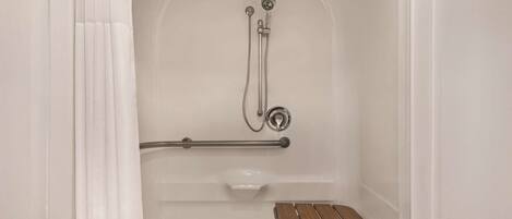 A bathroom with a shower, grab bar, and wooden bench.