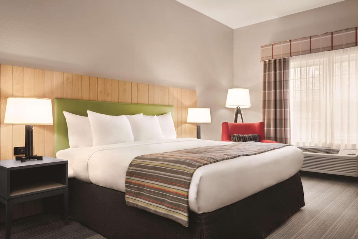 A hotel room with a large bed, two bedside tables with lamps, a red chair, and a window with curtains.