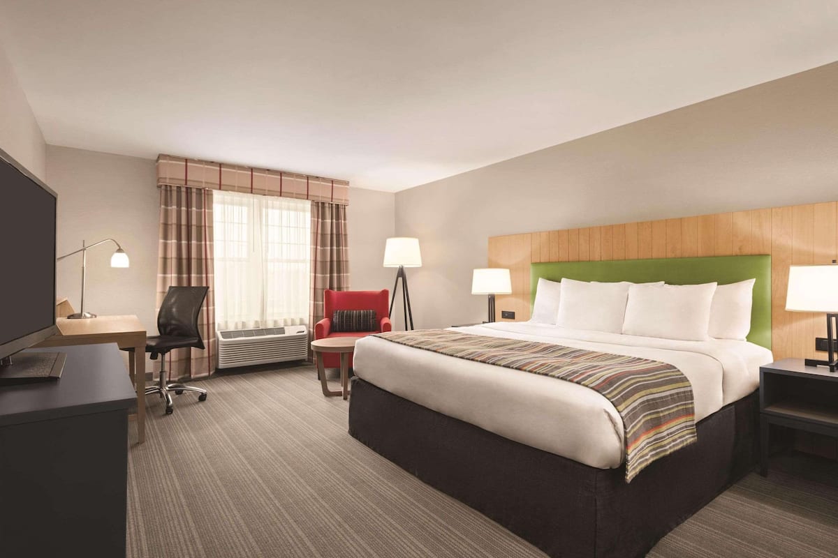 A hotel room with a large bed, a desk with a chair, a red armchair, two bedside lamps, and a television.