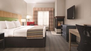 A hotel room with a bed, a desk, a chair, a TV, a fireplace, and a window with curtains.