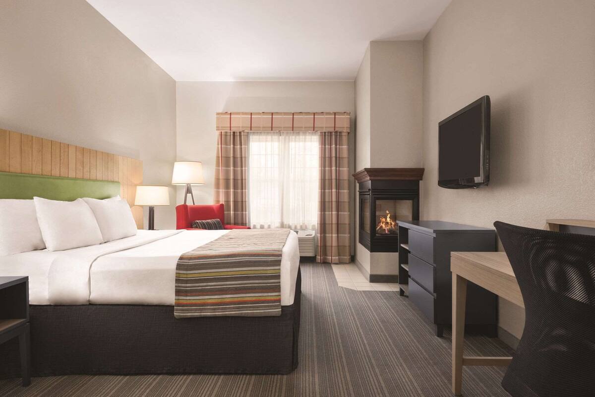 A hotel room with a bed, a desk, a chair, a TV, a fireplace, and a window with curtains.