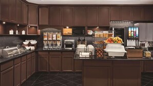 A modern kitchen with dark wood cabinets, a microwave, toaster, and a refrigerator. There are various food items and utensils on the counter.