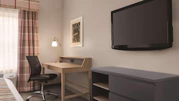 A hotel room with a bed, a desk with a chair, a television, and a framed picture on the wall.