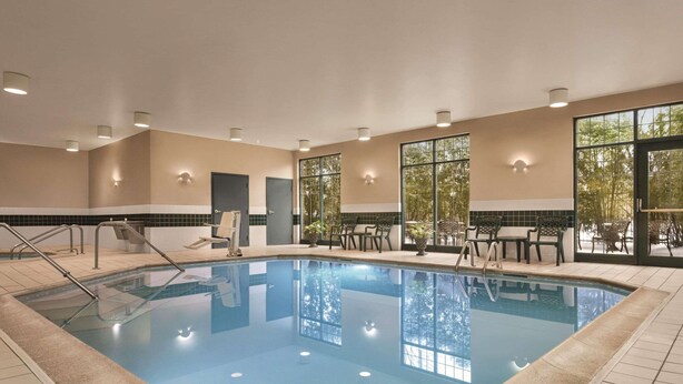 An indoor swimming pool with clear water, surrounded by tiled walls and a ceiling with recessed lighting.