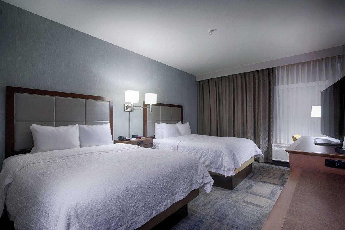 Une chambre d’hôtel avec deux lits, un bureau, une chaise, une télévision et une fenêtre avec des rideaux.
