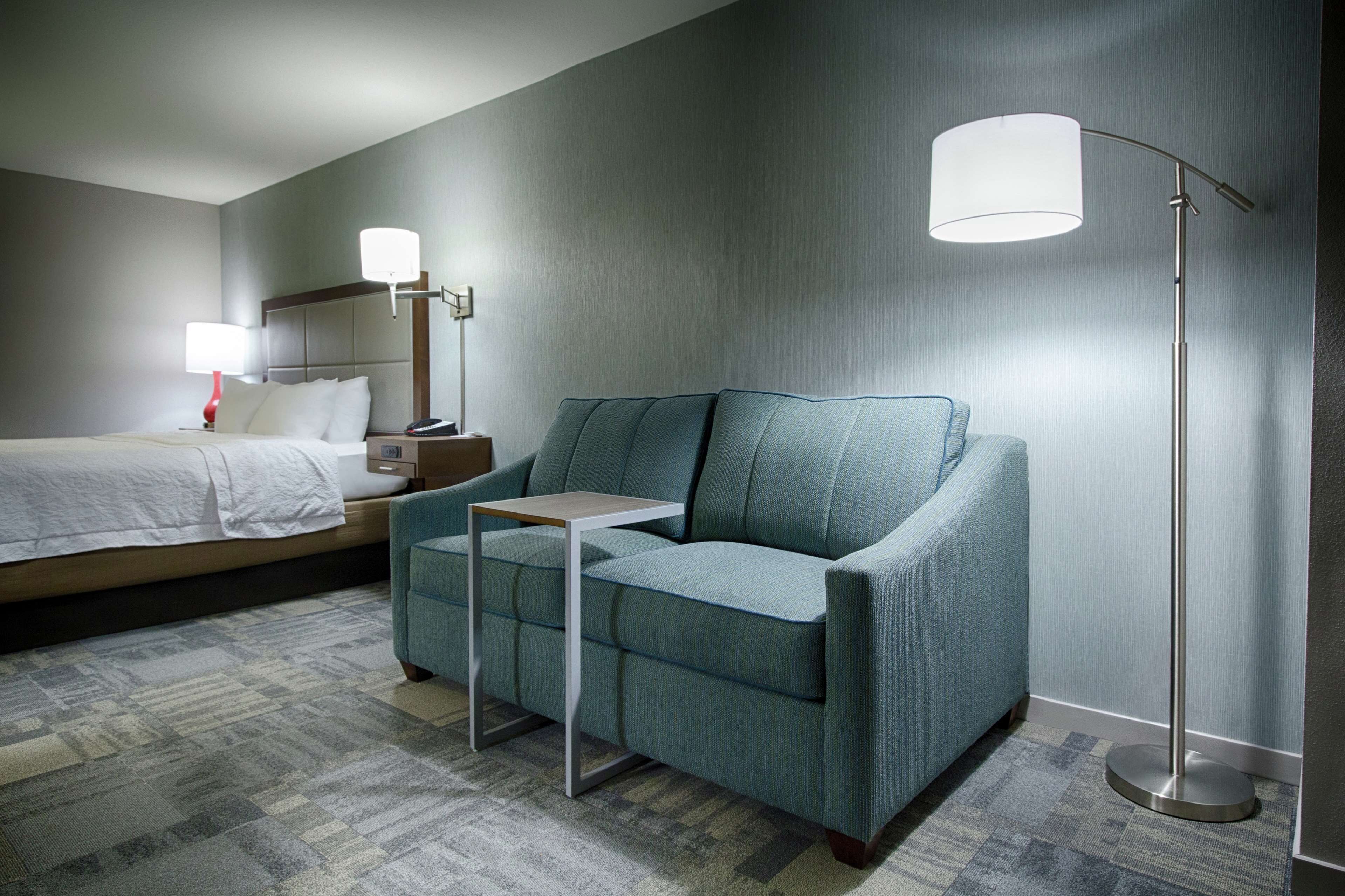 A hotel room with a bed, a sofa, a small table, and a floor lamp.