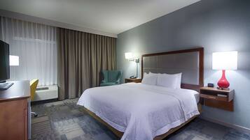 Habitación de hotel con una cama grande, un escritorio con computadora, una silla, un televisor y una lámpara.