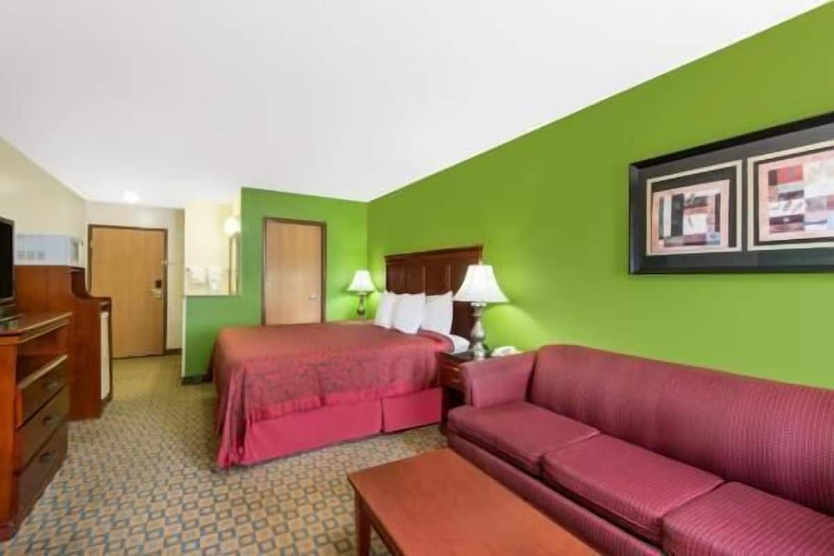 A hotel room with a bed, a sofa, a desk, and a door.