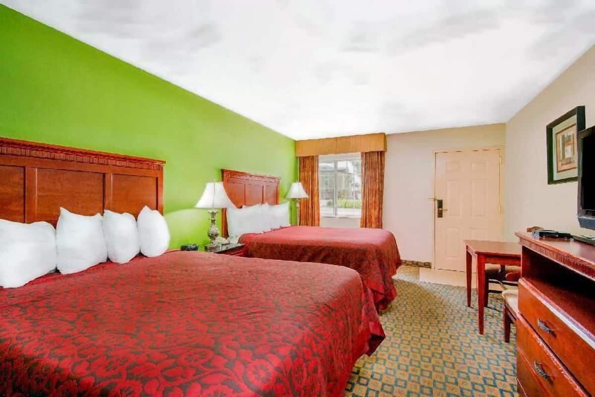 A hotel room with two beds, a television, a desk, and a window with curtains.