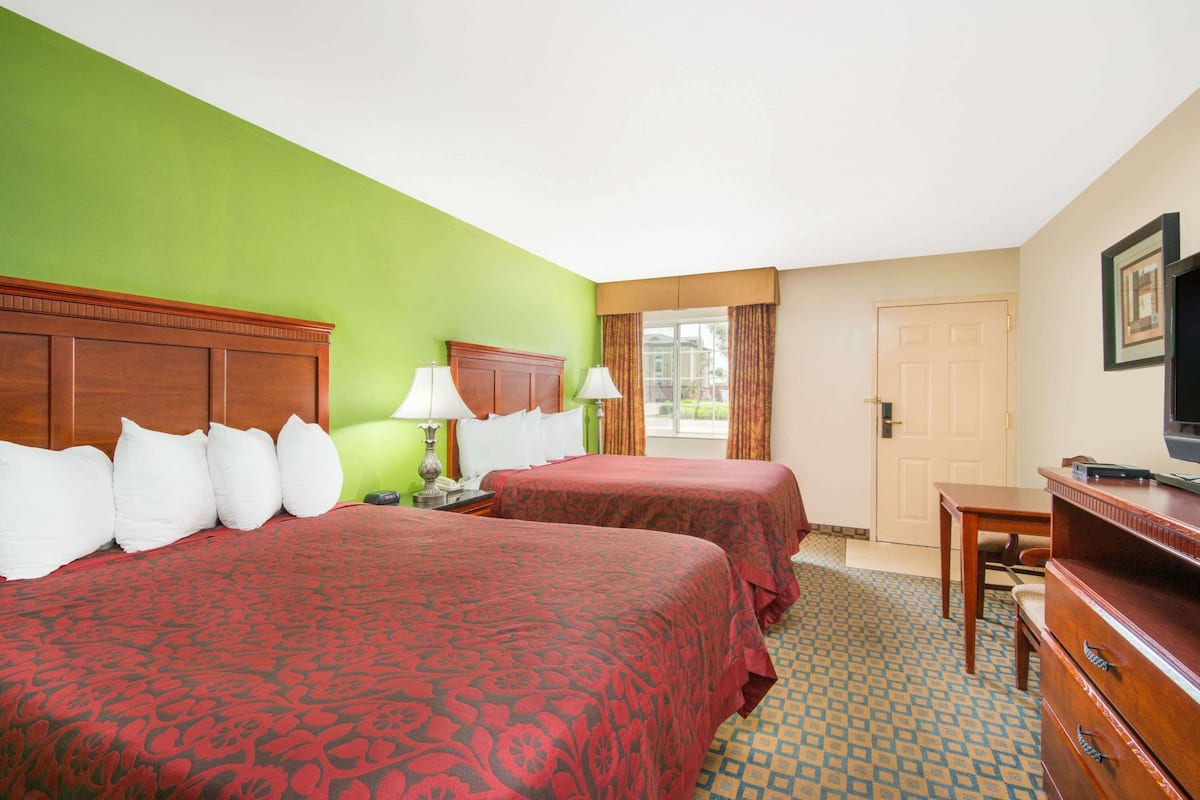 A hotel room with two beds, a desk, a television, and a window with curtains.