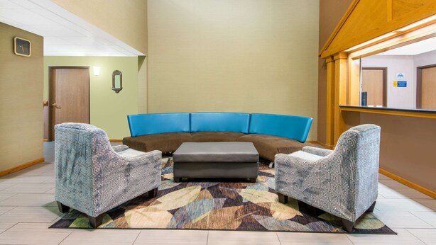 Una habitación con un sofá marrón, dos sillones estampados, un tapete con diseño y techo de madera.