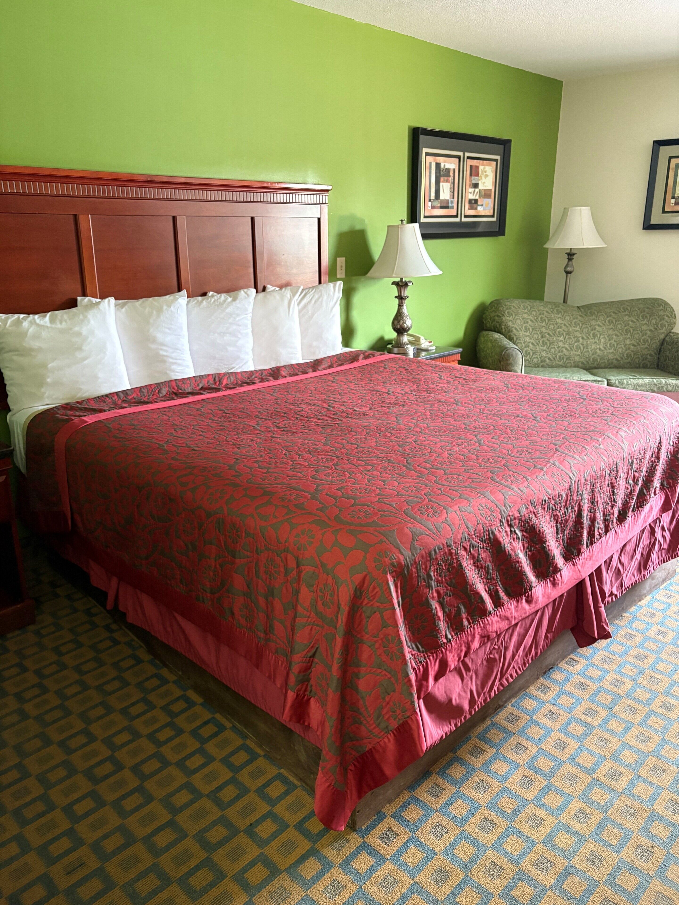 Habitación de hotel con una cama grande, cabecera de madera, pared verde, suelo estampado y un sillón verde.