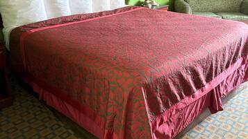 A hotel room with a large bed, a wooden headboard, a green wall, a patterned floor, and a green armchair.
