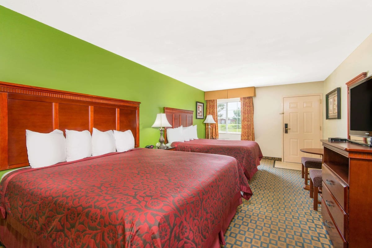 A hotel room with two beds, a television, a desk, and a chair.