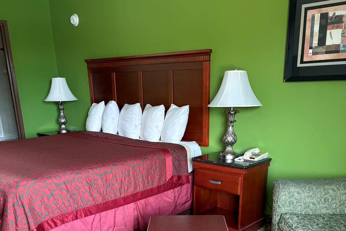 A hotel room with a bed, bedside tables, a nightstand, a desk, and a patterned carpet.
