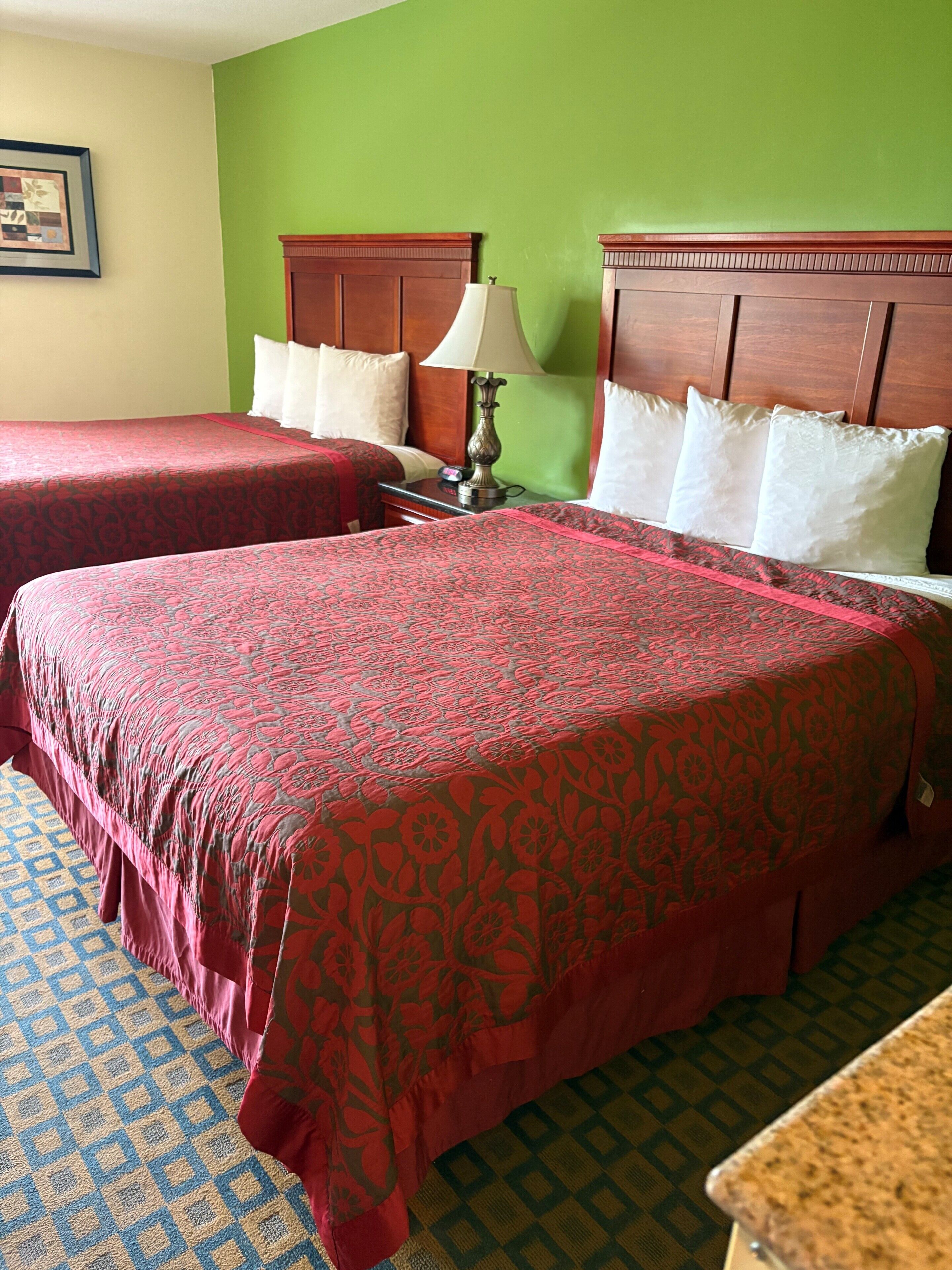 Una habitación de hotel con dos camas, una mesita de noche con lámpara y una alfombra estampada.