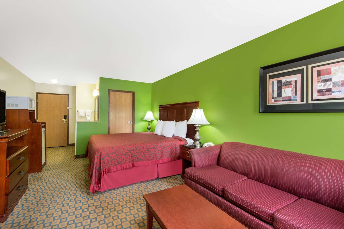 A hotel room with a bed, a sofa, a desk with a lamp, and a framed picture on the wall.