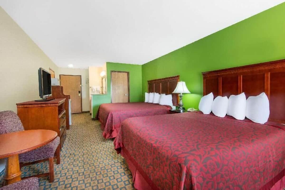 A hotel room with two beds, a desk, a chair, a television, and a lamp.