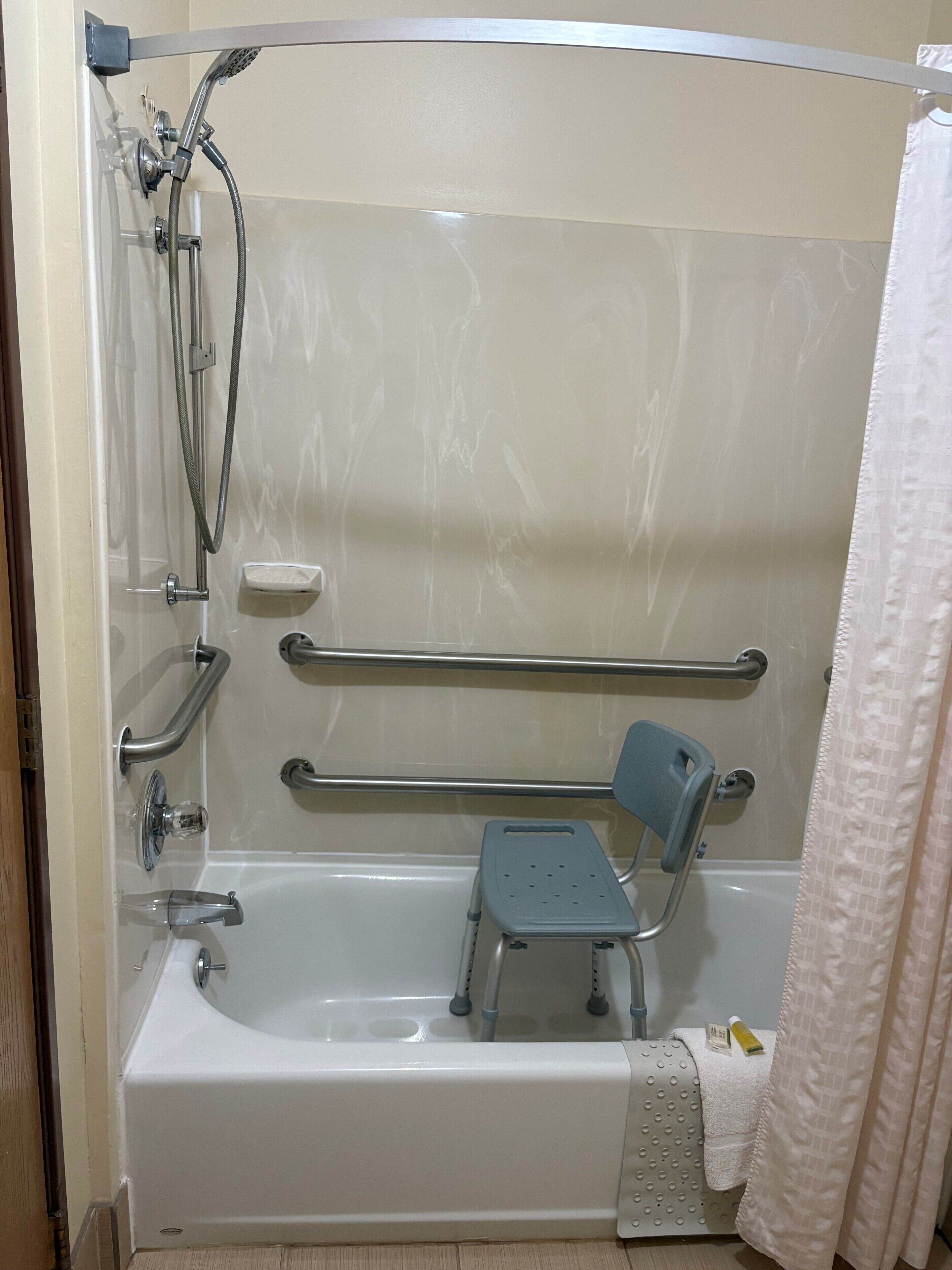 Une baignoire équipée d’un pommeau de douche, de barres d’appui et d’un petit marchepied.