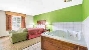 Habitación de hotel con pared verde, una bañera grande, un sofá, una cama con manta roja y una ventana con cortinas.