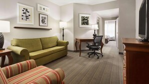 A hotel room with a green sofa, a striped armchair, a desk with a chair, and a television on a wooden cabinet. - Country Inn & Suites by Radisson, Lexington, KY (Lexington)