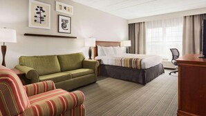 A hotel room with a bed, a green sofa, a striped armchair, and a desk with a lamp. - Country Inn & Suites by Radisson, Lexington, KY (Lexington)