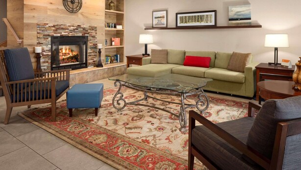 A cozy living room with a fireplace, a green sofa, a blue armchair, and a glass coffee table. - Country Inn & Suites by Radisson, Lexington, KY (Lexington)