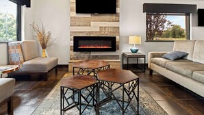 A modern living room with a fireplace, a flat-screen TV mounted on a wooden wall, and a large window providing a view of the outdoors. - Best Western Paducah Inn (Paducah)