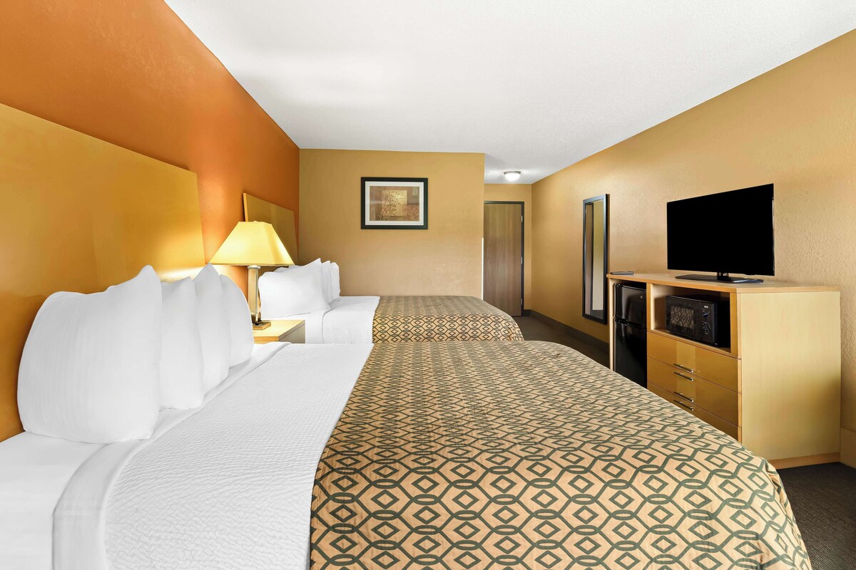 A hotel room with two beds, a TV, a microwave, and a desk with a lamp.