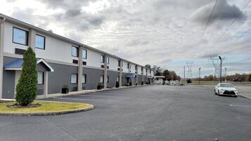 A modern hotel with a row of rooms, a parking lot, and a white car parked in the lot.