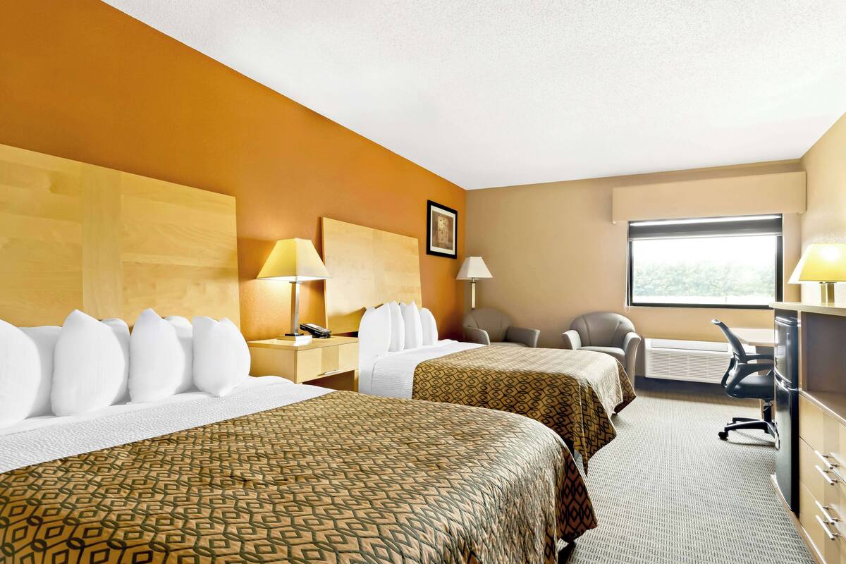 Une chambre d’hôtel avec deux lits, un bureau, une chaise et une fenêtre.