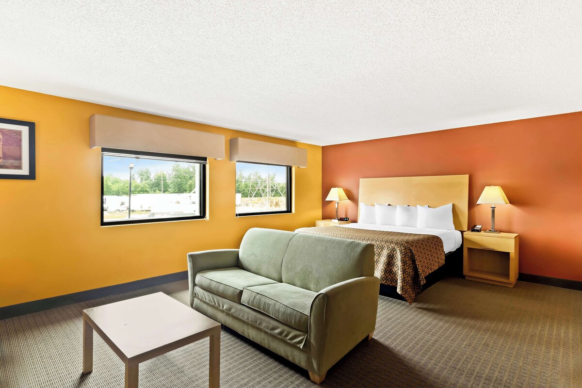 A hotel room with a bed, a green sofa, a small table, and two windows with blinds.