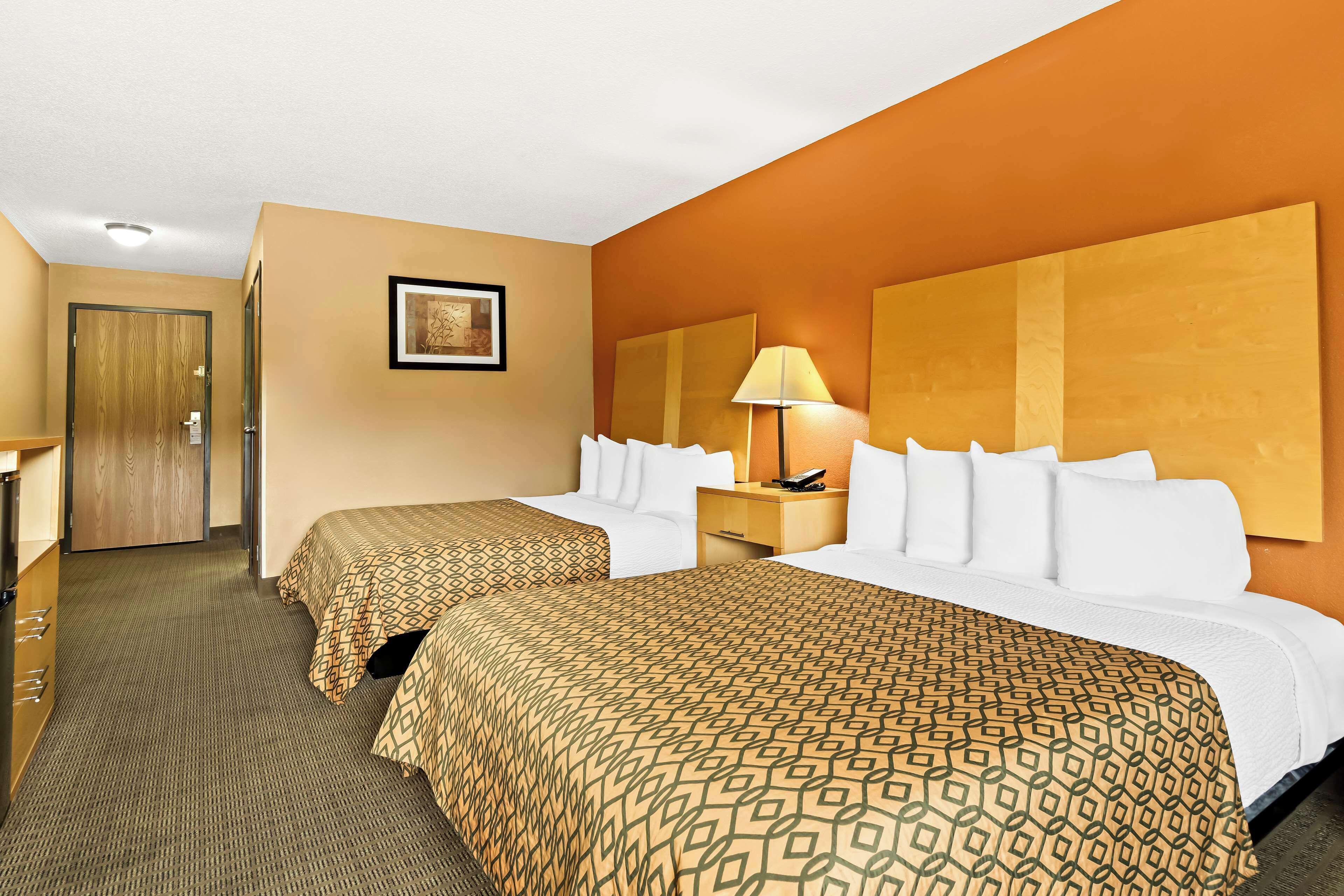 A hotel room with two beds, a desk, a lamp, and a framed picture on the wall.