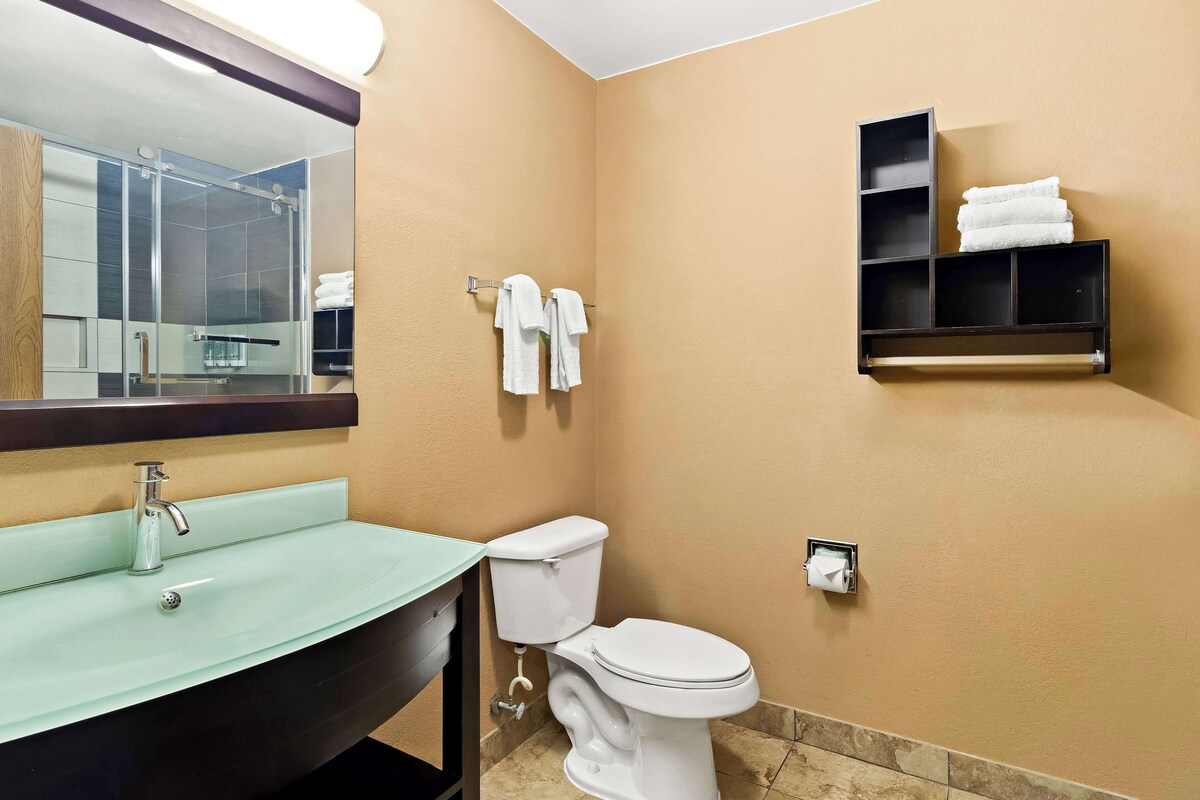 A bathroom with a glass sink, a toilet, a towel rack, and a shelf with towels.
