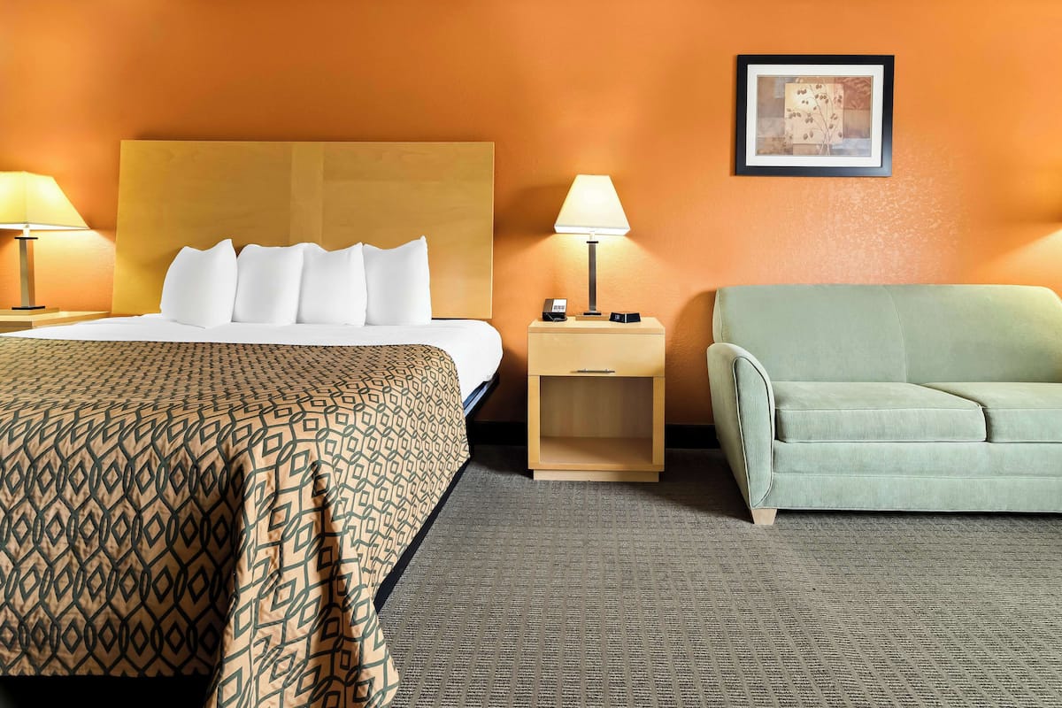 Une chambre d’hôtel avec un lit, une table de chevet, une lampe, un canapé et un tableau encadré au mur.