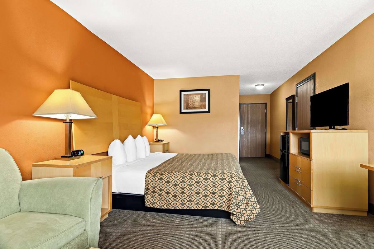 Une chambre d’hôtel comprenant un lit, deux lampes de chevet, un bureau avec une lampe, une télévision et une armoire.