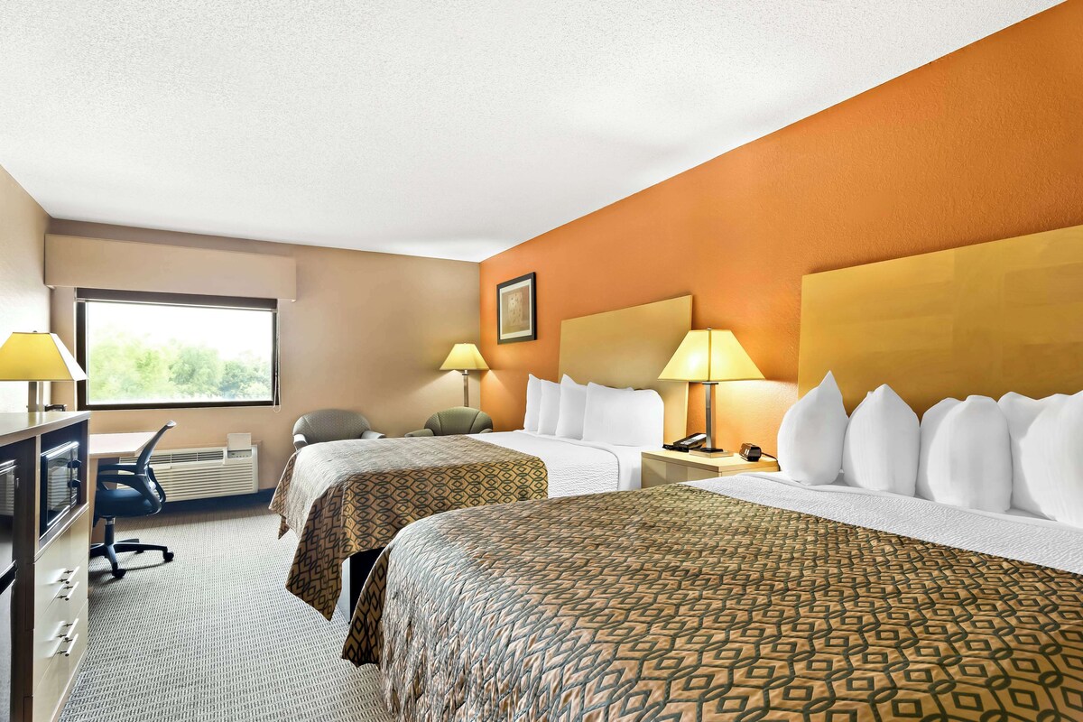 A hotel room with two beds, a desk, a chair, and a window.