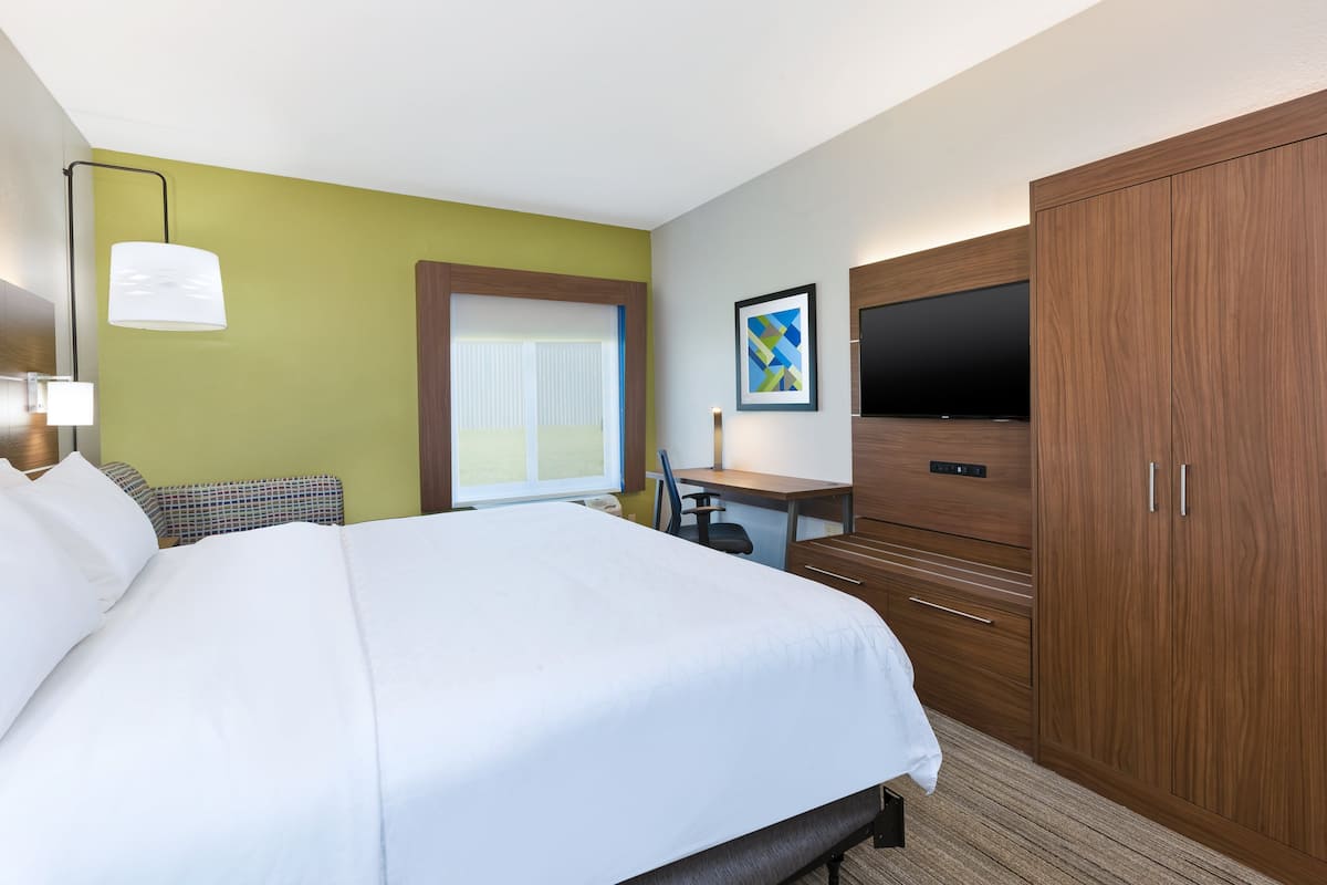 A hotel room with a large bed, a desk, a television, and a wardrobe.