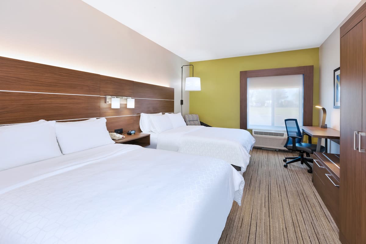 A hotel room with two beds, a desk, a chair, and a large window.