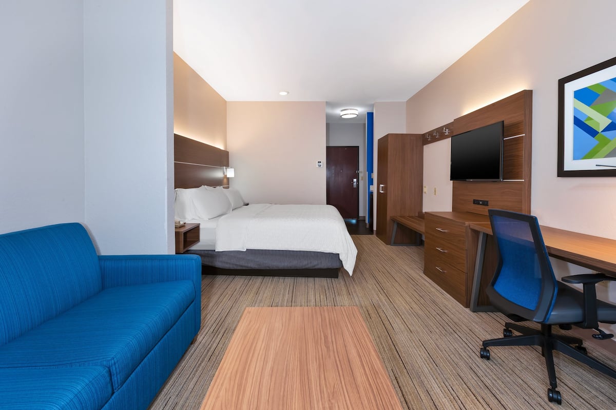 A hotel room with a bed, a desk with a chair, a sofa, and a TV on the wall.